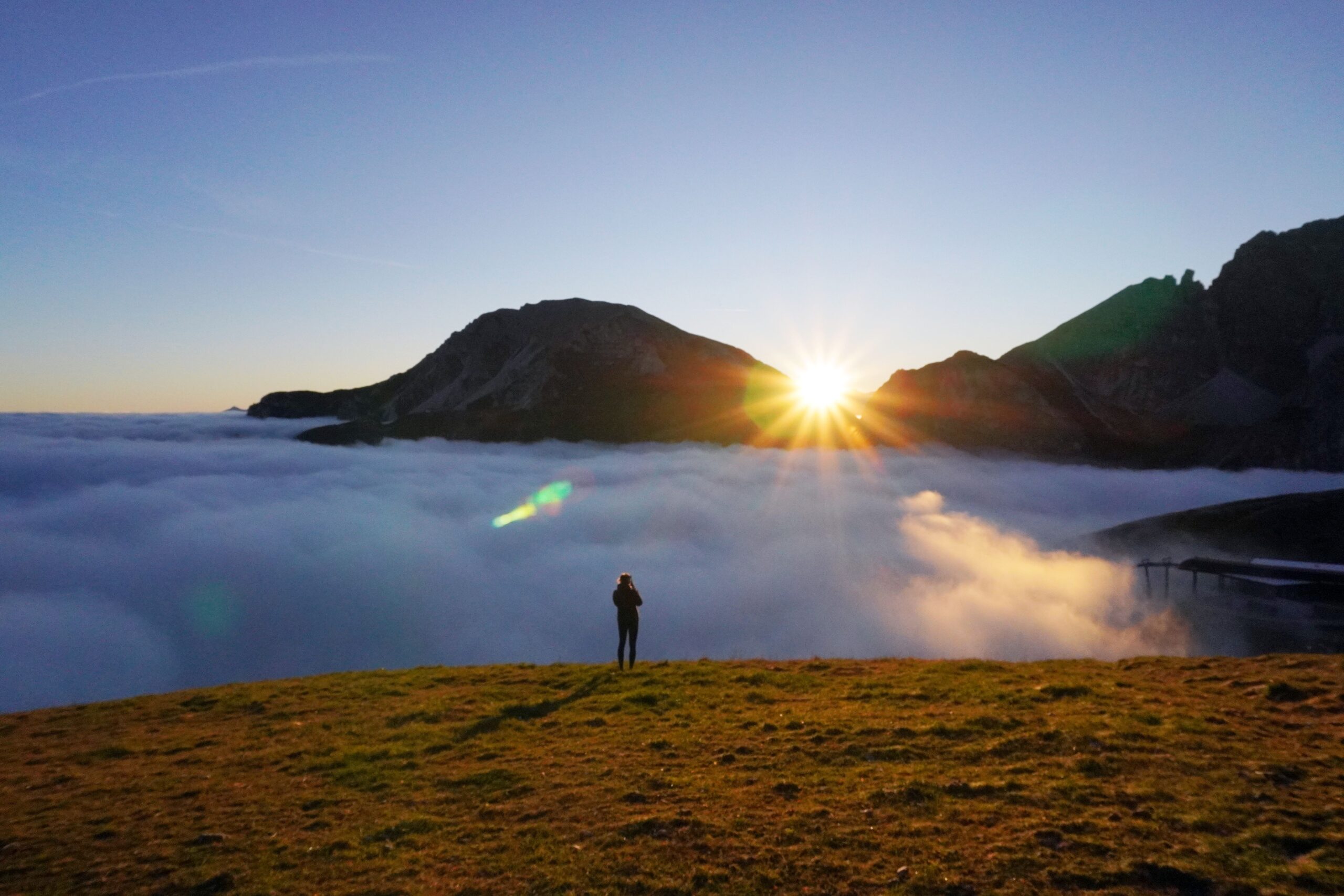 Silhouette of a person watching sunrise over Innsbruck mountains with clouds below.